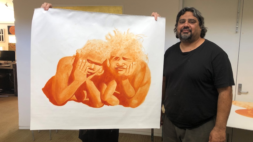 A man holds up a painting of two Indigenous people.