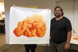 A man holds up a painting of two Indigenous people.