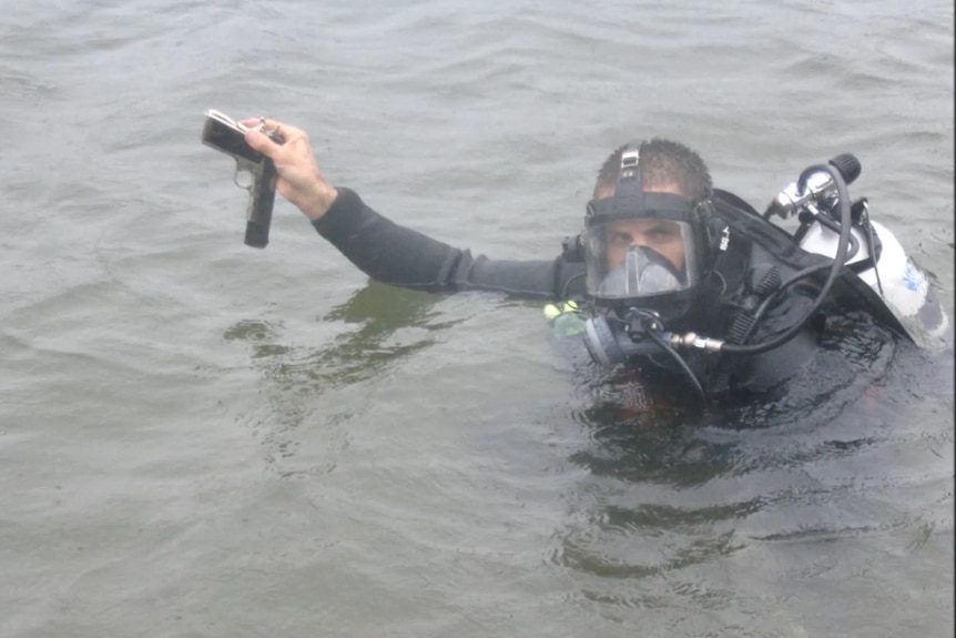 A Queensland police diver holds up a firearm during a search in muddy waters.