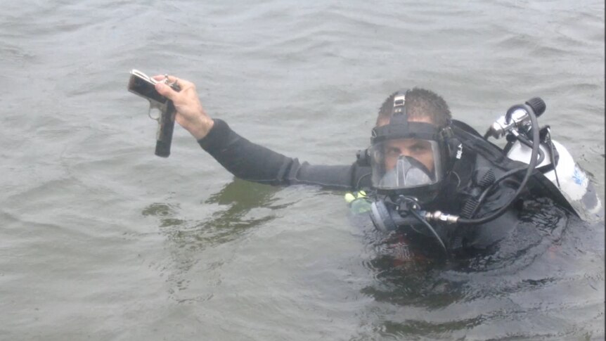 A Queensland police diver holds up a firearm during a search in muddy waters.
