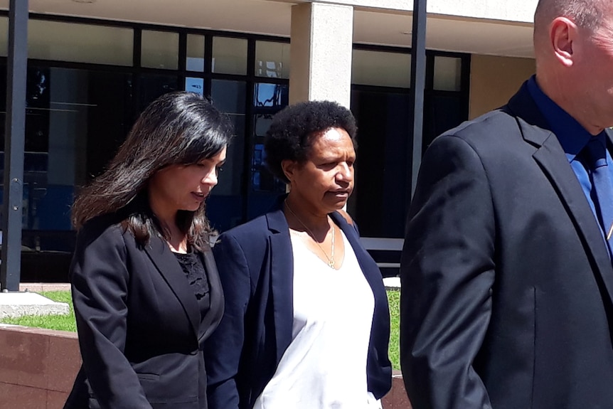 A woman in white shirt and dark blazer walks between two lawyers out of the Cairns courthouse
