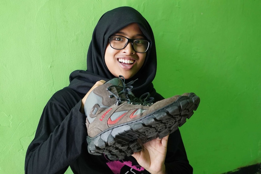Nur Dhania holds up a pair of old sneakers