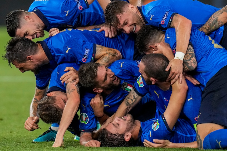 A number of Italian players form a human pile as they celebrate a goal.