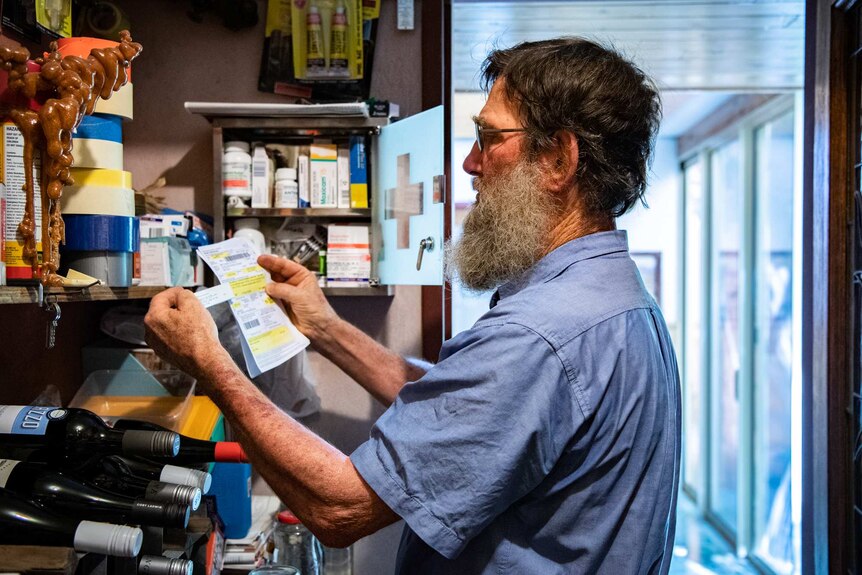Don Firth compares a doctor’s prescription with a box of medication in front of a packed medicine cabinet.