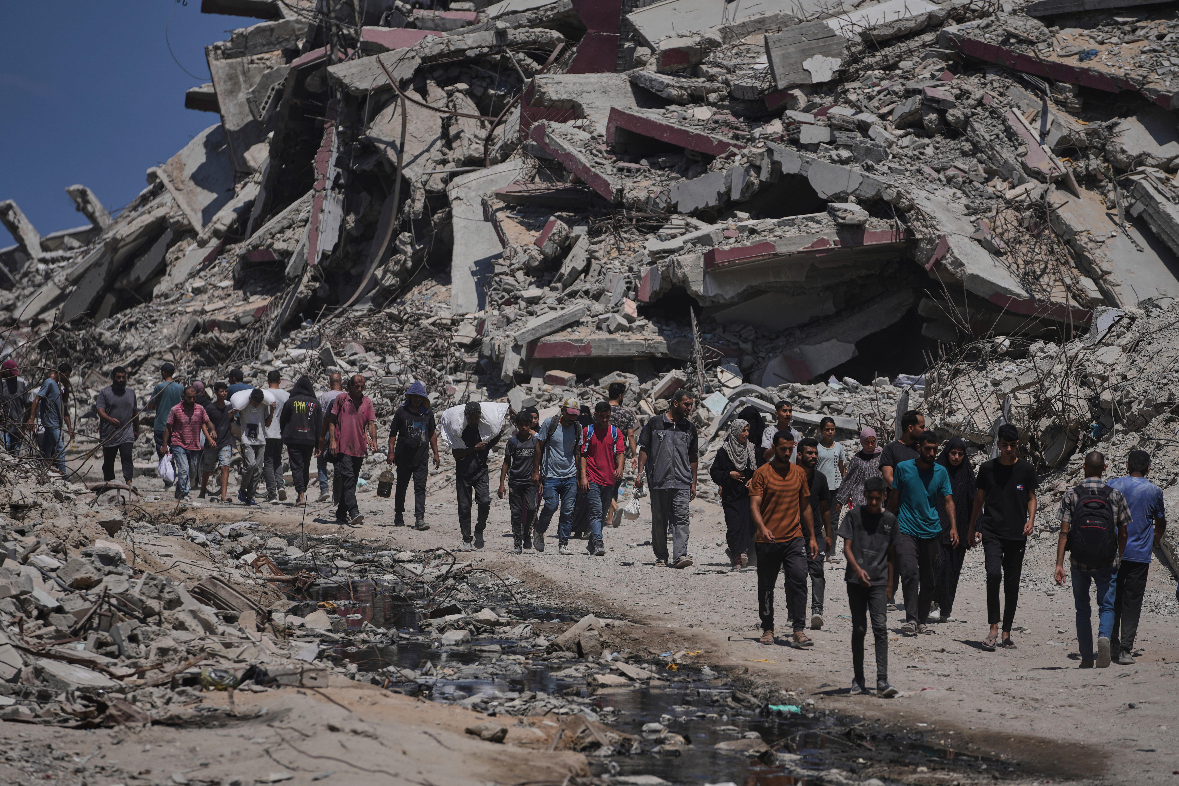 A line of Palestinian men and women walking in single-file along a dirt track next to a large mound of concrete debris