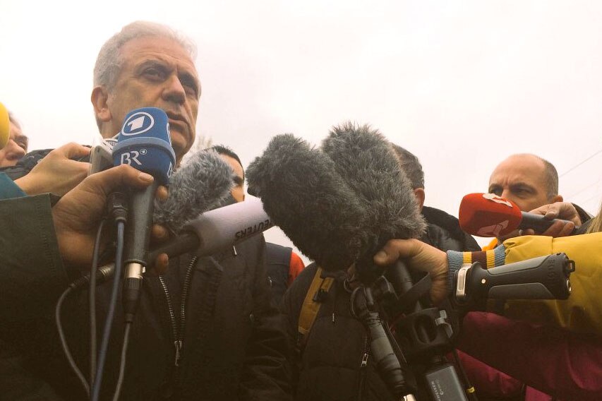 Low down view of Dimitris Avramopoulos speaking in front of microphones at outdoor location.