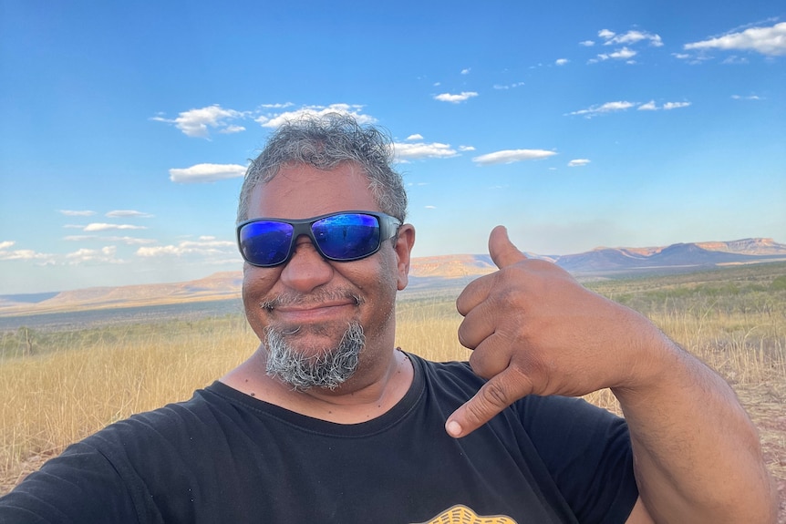 An Indigenous man wearing sunglasses smiles, with wetlands behind him.