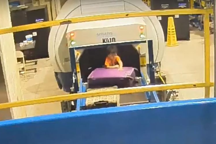 A toddler stuck on a conveyor belt tries to climb over luggage to get away from a baggage screening machine at Atlanta airport.
