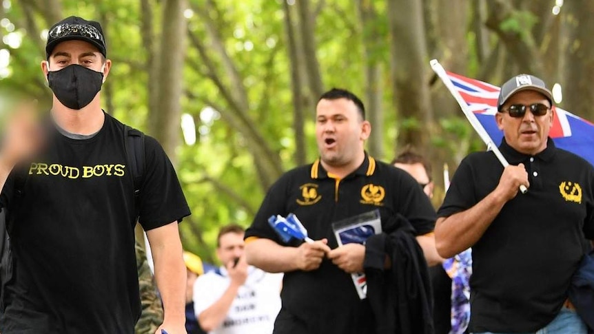 Men in black tops with the Proud Boys name and logo walk down St Kilda Road.