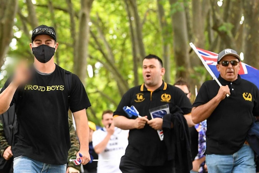 Men in black tops with the Proud Boys name and logo walk down St Kilda Road.