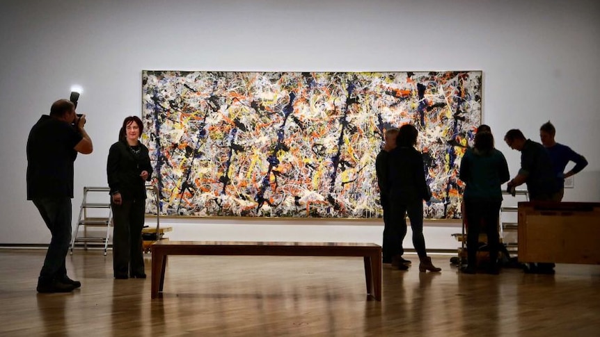 An abstract painting in a gallery surrounded by people
