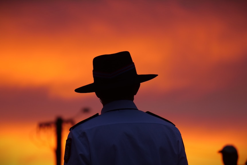 A man's outline in a slouch hat with an orange sunrise in the background.