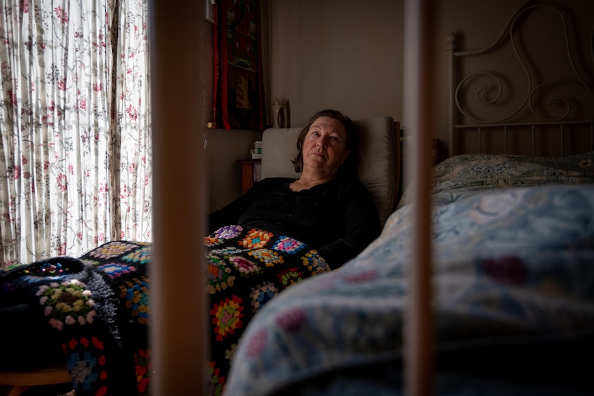 A middle-aged white woman lying in bed looking exhausted. She is photographed through a bed frame
