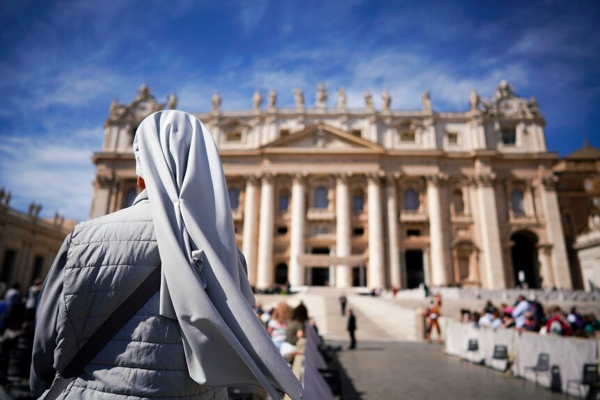 A Catholic nun in a habit waits outside of St Peter's Basilica on a clear day for a Papal address