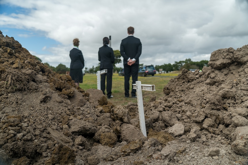 Three people in dark suits stand near graves.