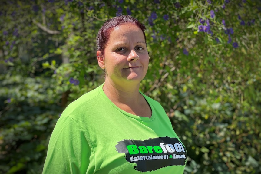 A woman wearing a bright green shirt stands in front of a garden