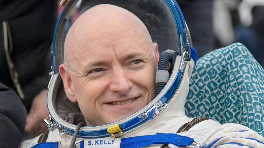Astronaut Scott Kelly sits on ground wearing his suit