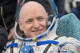 Astronaut Scott Kelly sits on ground wearing his suit