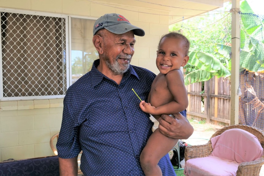Older Torres Strait Islander man holding a baby wearing nappies, both smiling