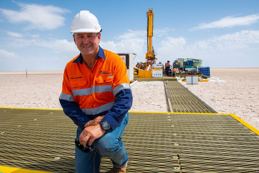 A man in an orange jumpsuit kneels on a platform.