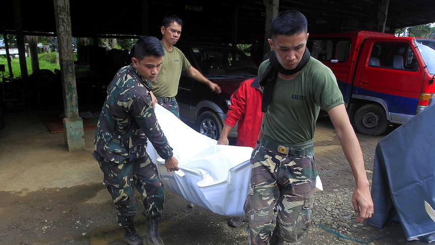 Two soldiers carry a body in a bag.