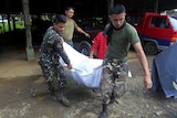 Two soldiers carry a body in a bag.