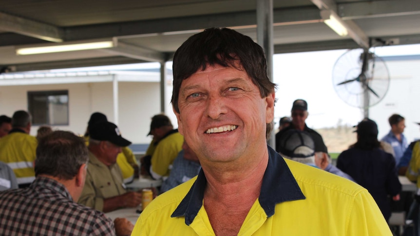 A dark-haired man wearing high-vis smiles broadly in a canteen at a mining site.