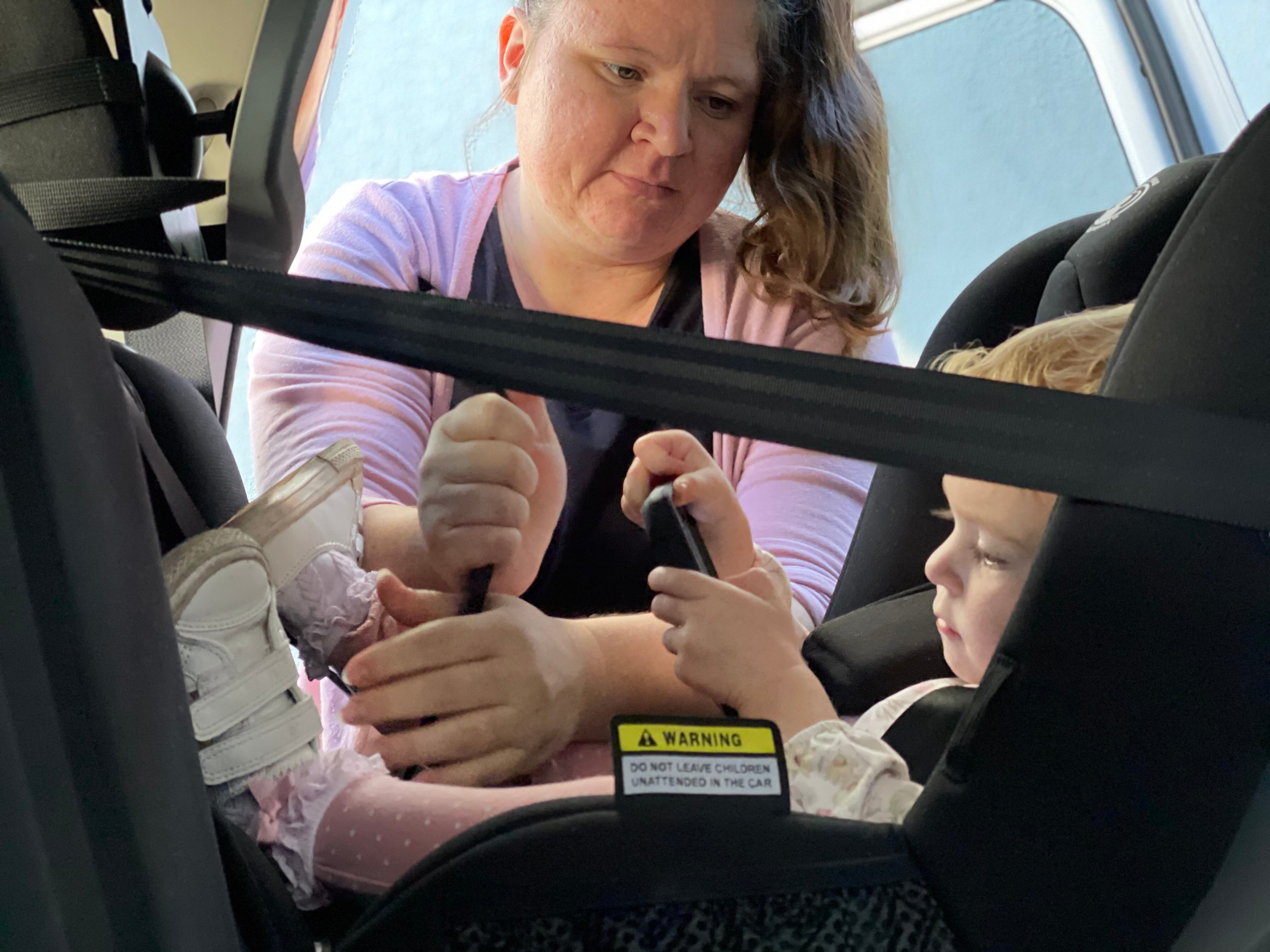 A woman tightens a strap of her daughter's car seat.