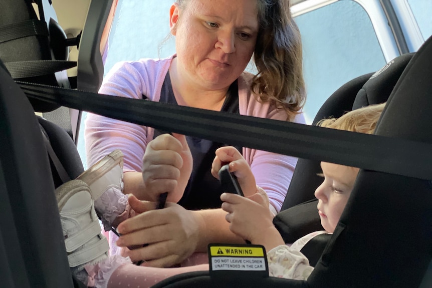 A woman tightens a strap of her daughter's car seat.
