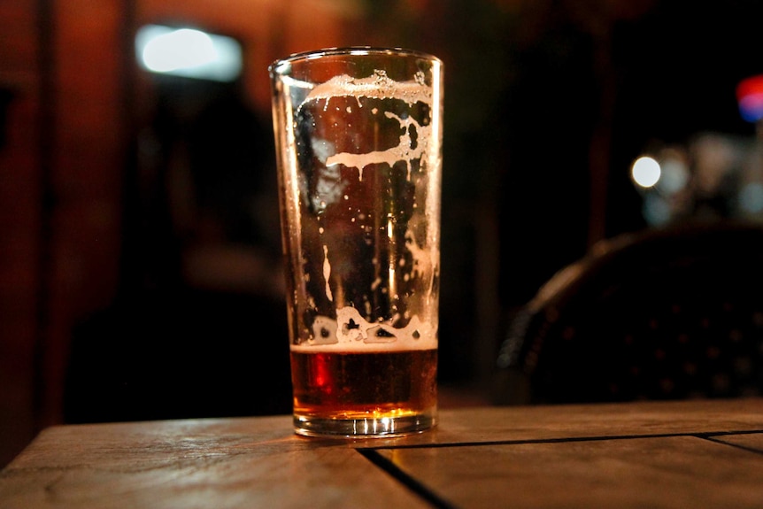 Vaso de cerveza casi vacío sobre una mesa de madera por la noche en una taberna al aire libre