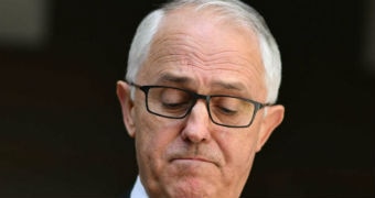 Malcolm Turnbull frowns and looks downwards during a press conference. He is wearing black-rimmed glasses.