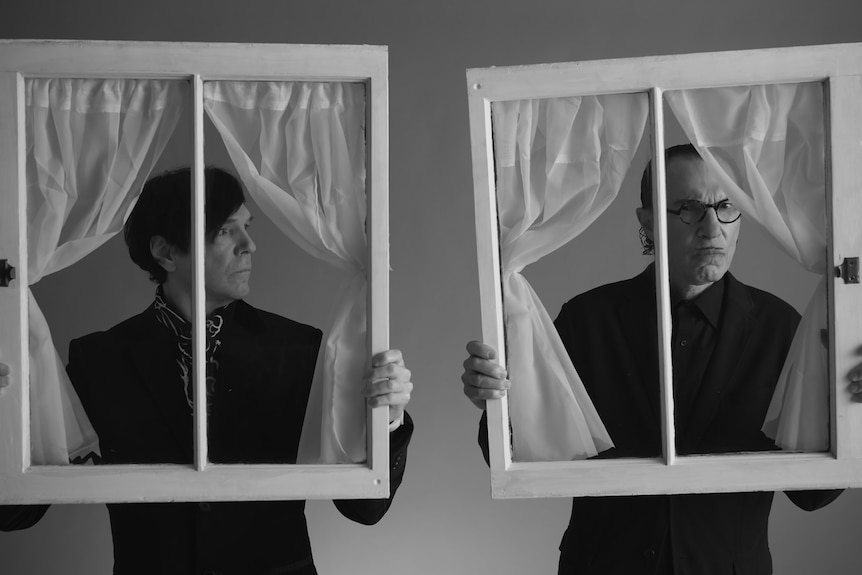 Black and white image of Russell Mael and Ron Mael holding up prop windows with curtains in The Sparks Brothers
