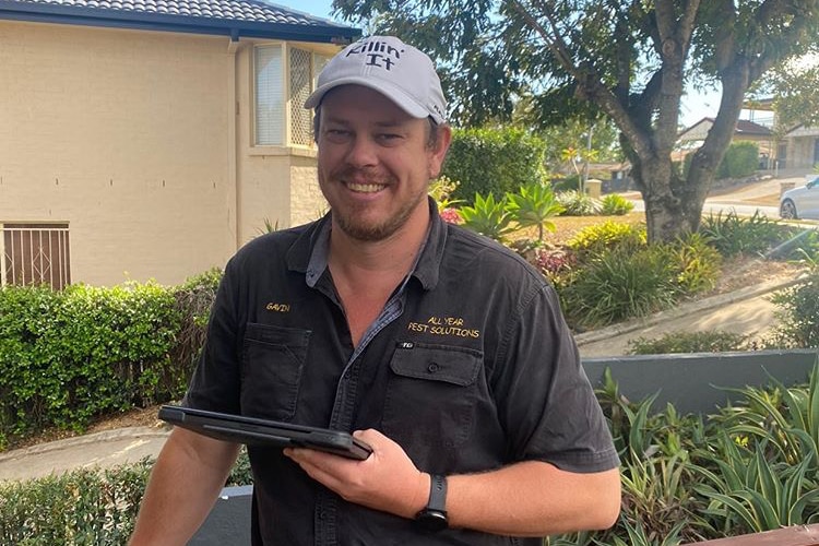 A man stands smiling on a deck, holding a tablet. 