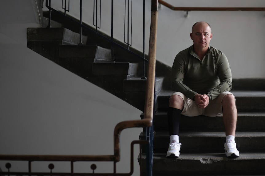 Man sits on stairs as he looks directly into the camera.