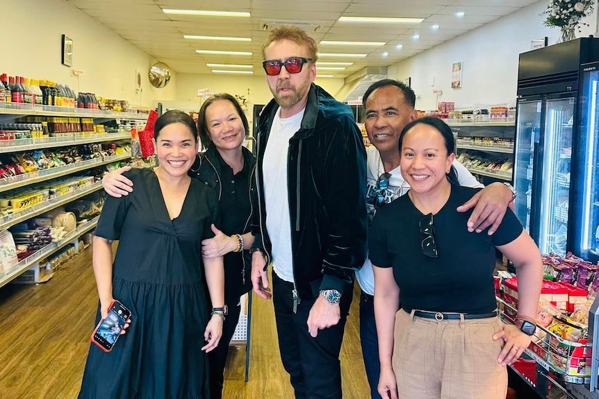 Five people standing in a asia grocery store. Man in the middle wearing red tinged glasses.