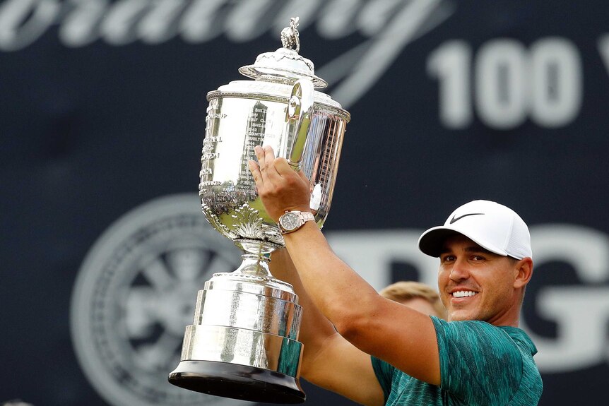 Brooks Koepka lifts a large silver cup.