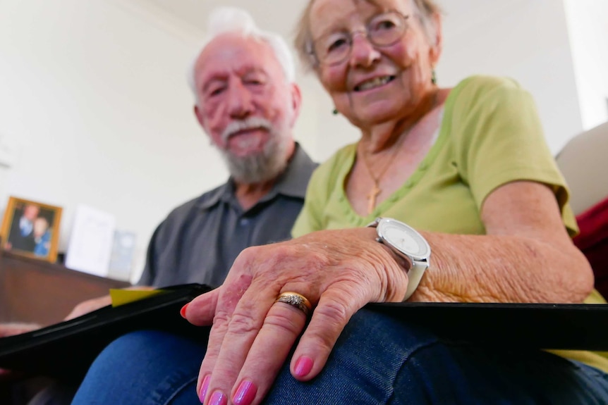 Focus on a wedding and engagement ring on a woman's hand, with woman and man just out of focus.