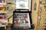 A local newspaper on the stand in a newsagent, surrounded by other items like sweets and magazines