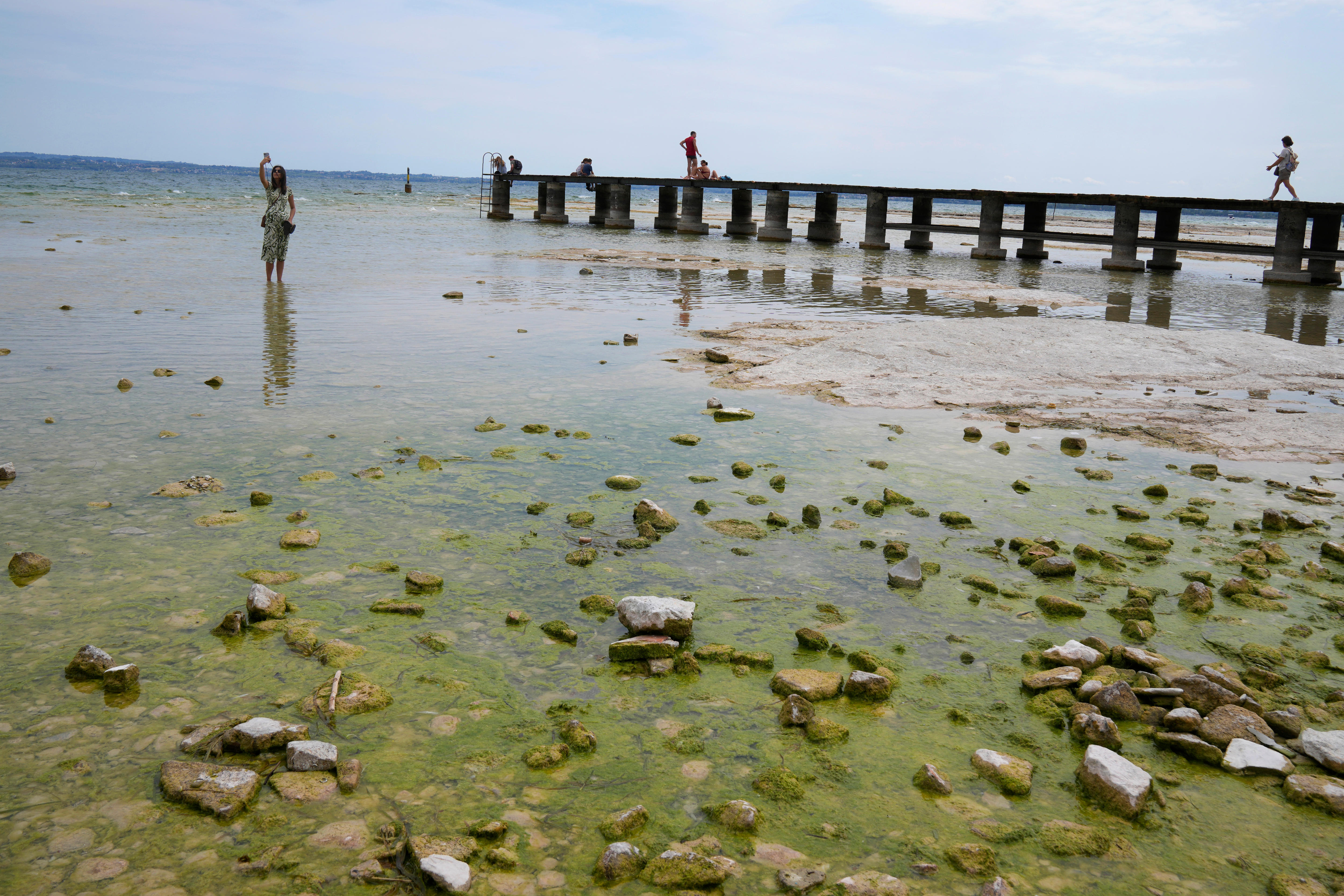 A woman takes a selfie in water near a pier at Lake Garda