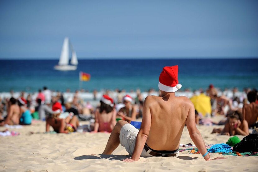 Tourist sitting on Bondi Beach wearing a Santa hat to depict how to find joy during the draining holiday season.