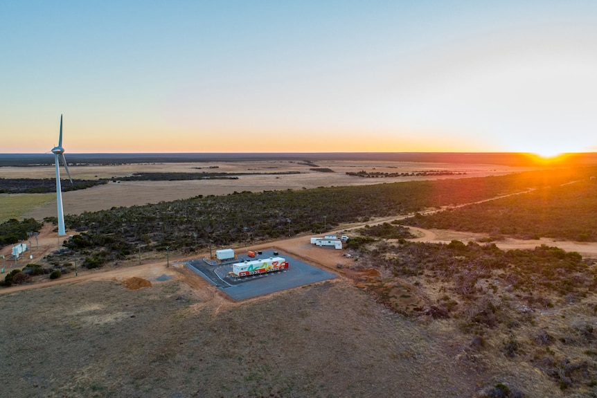 An aerial view of a wind turbine and a shipping crate-sized battery.