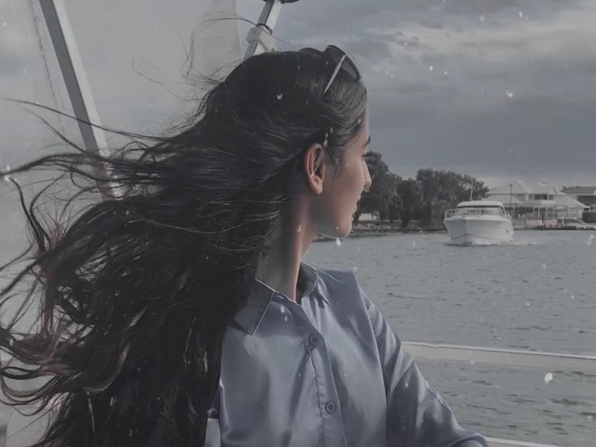 Woman with long black hair flowing look over water while sitting on boat.