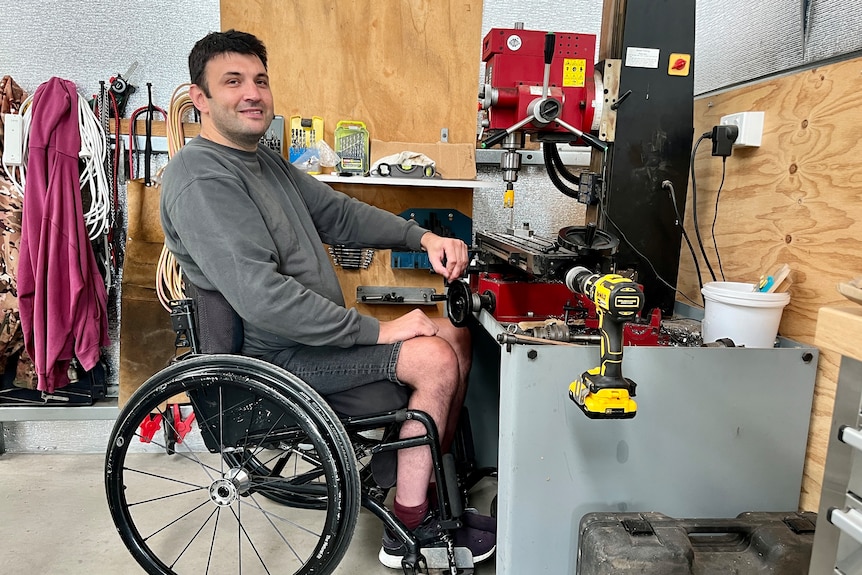 A man in a wheelchair in front of a drill press in a workshop.