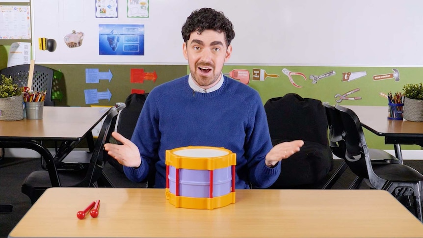 Male teacher sits at desk with toy drum