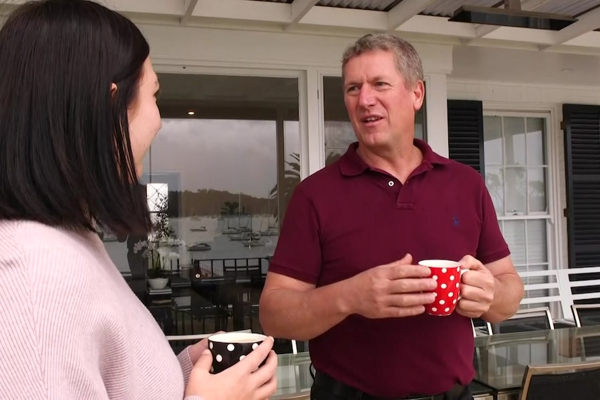 A middle-aged man speaks to a younger woman while holding a mug.