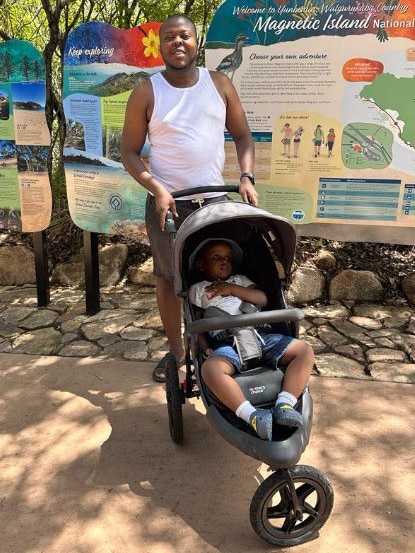 a man stands with his son in a stroller in front of a sign that says magnetic island