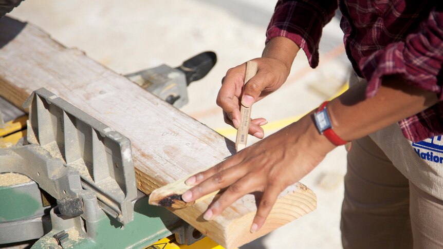 A close up of a female carpenter's hand marking up a piece of timber.