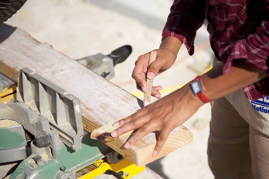 A close up of a female carpenter's hand marking up a piece of timber.