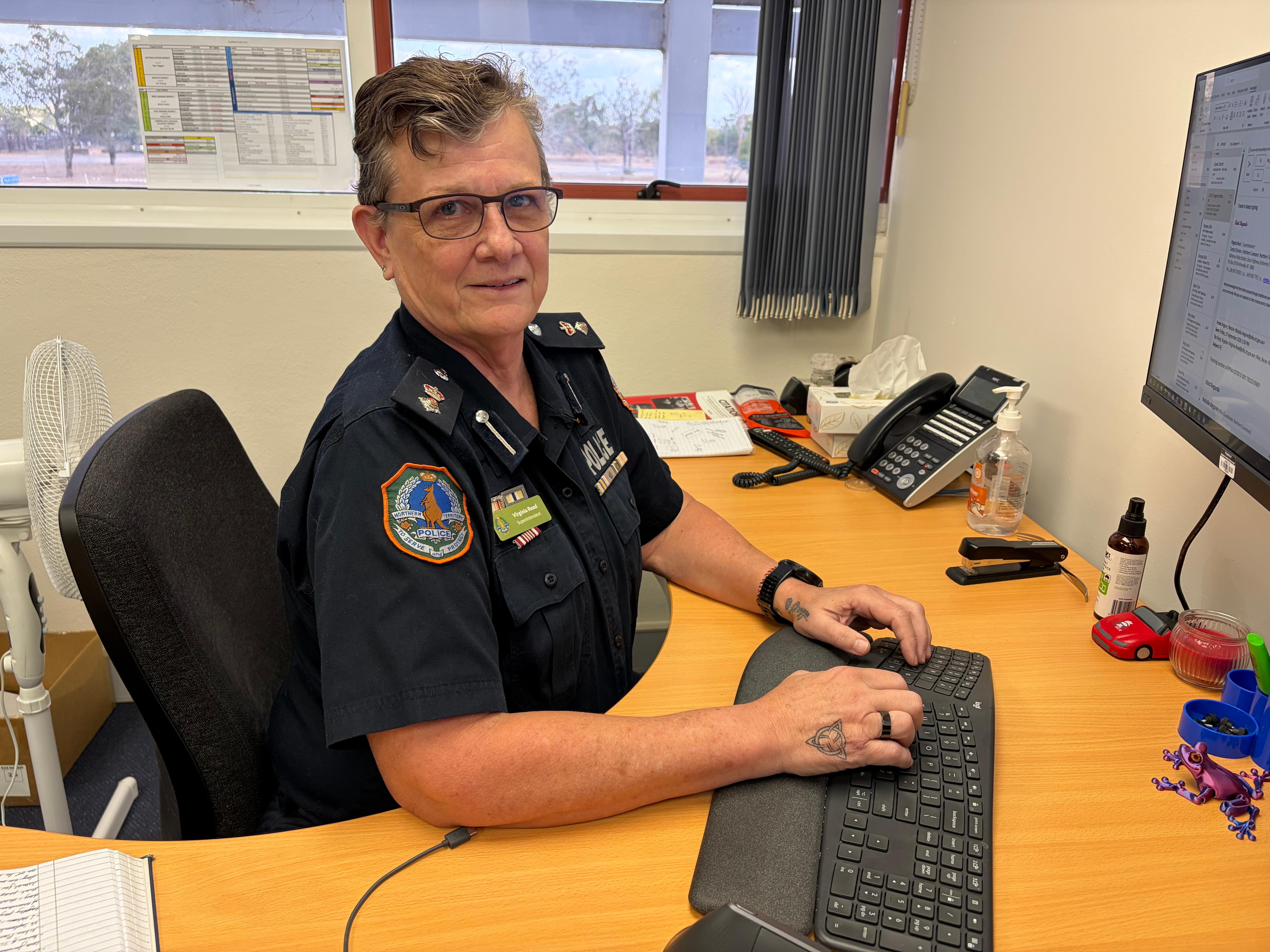 Female police officer Virginia Read sits at desk in front of computer wearing a neutral facial expression.