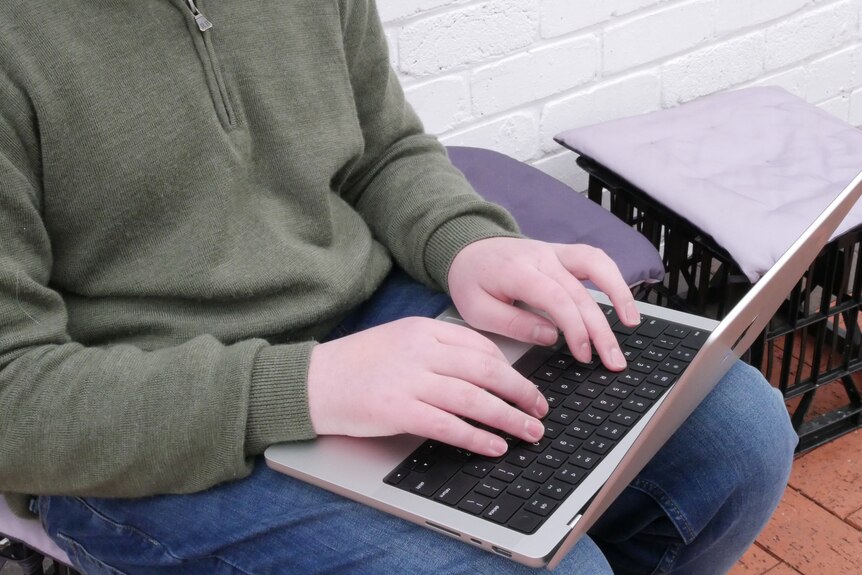 Hands typing on a laptop balanced on a lap